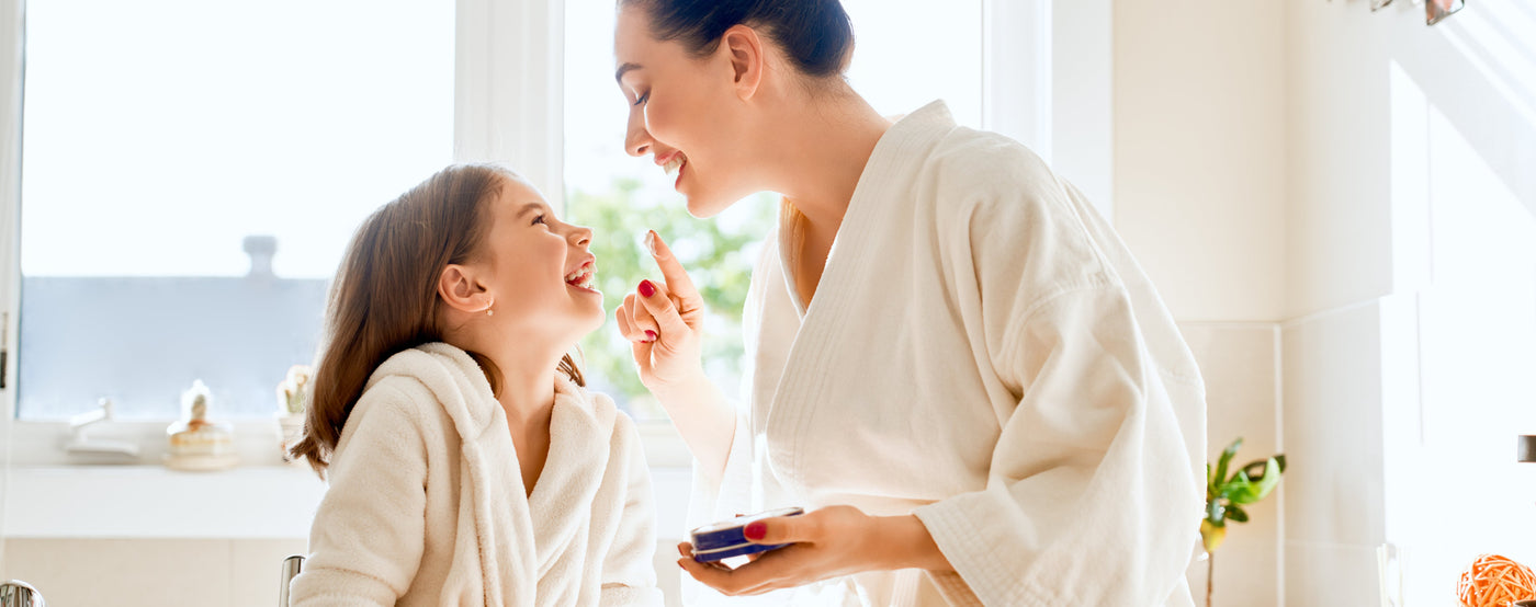 Mother and daughter in bath room with body care lotions and skincare