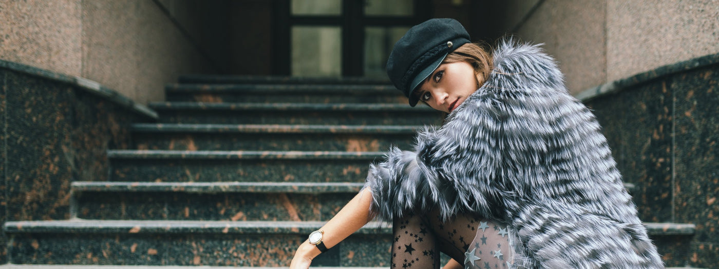 lady in grey fur coat and black baker boy hat sat on stepd 