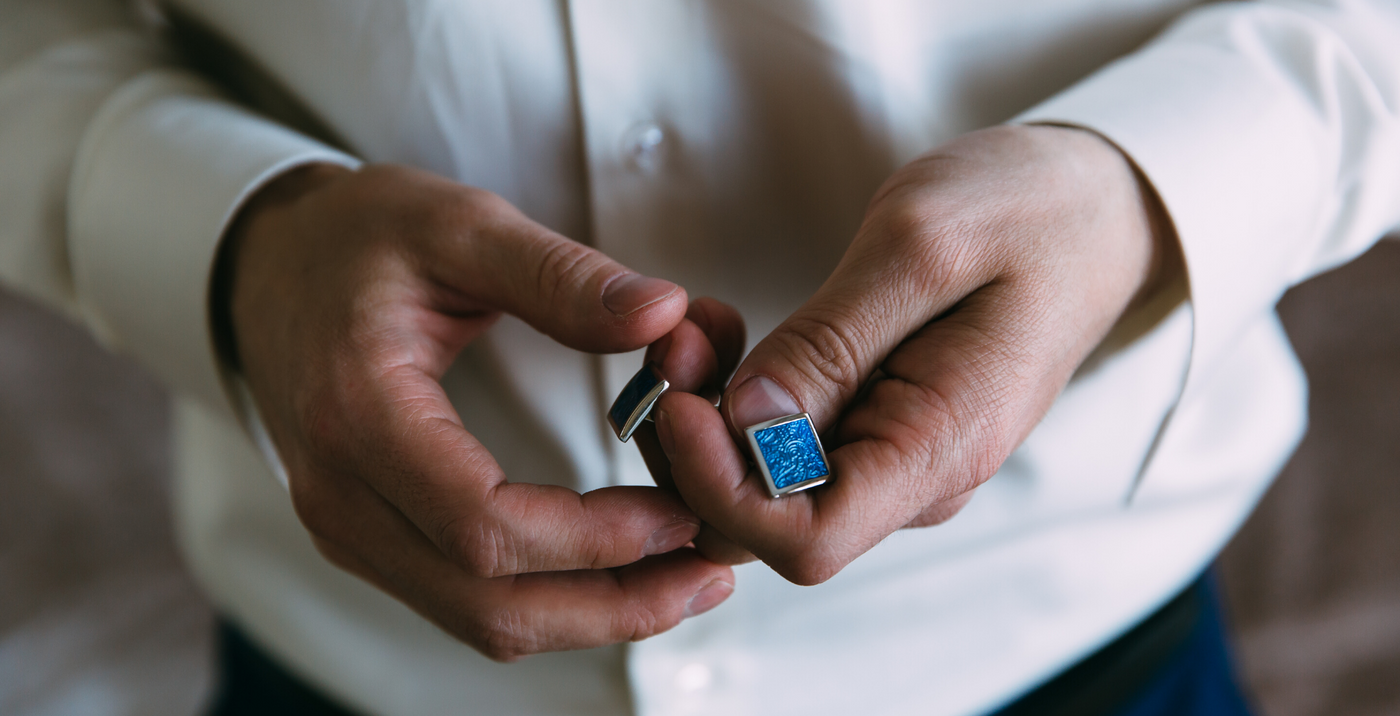 Man in a white shirt holding a pair of blue cufflinks